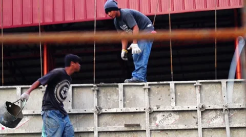 Worker toss up a bucket of concrete to other worker above Stock Footage