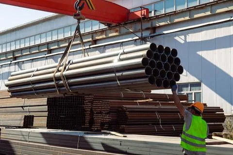 Worker transporting stack of metal pipes with gantry crane Stock Photos