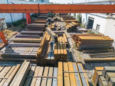 Worker transporting stack of metal pipes with gantry crane Stockfoto's
