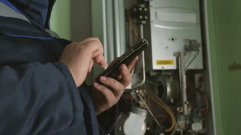 Worker typing on smartphone against gas-fire boiler Stockbeeldmateriaal 87762256