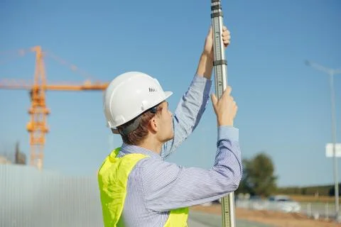 Worker is unfolding leveling rod on construction site. Stock Photos