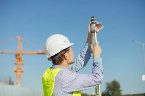 Worker is unfolding leveling rod on construction site. Stock Photos