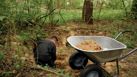 Worker in uniform digs a hole with a shovel in the forest and extracts sand Stock Footage 130168816