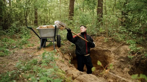 Worker in uniform digs a hole with a shovel in the forest and extracts sand Stock Footage 130168956