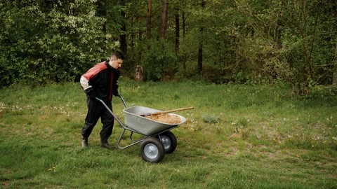 Worker in uniform going with wheelbarrow in the forest with sand Stock Footage 130169047