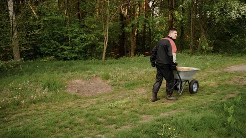 Worker in uniform going with wheelbarrow in the forest with sand Stock Footage 130169070