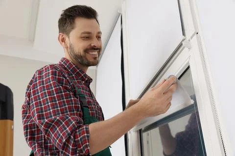 Worker in uniform installing roller window blind indoors Stock Photos