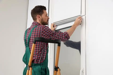 Worker in uniform installing roller window blind indoors Stock Photos
