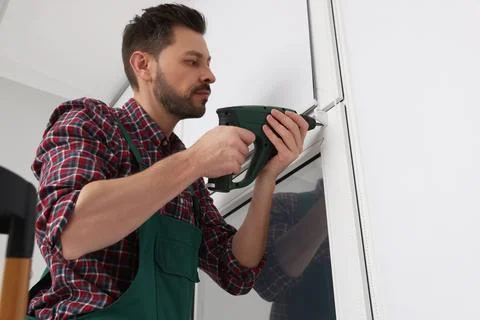 Worker in uniform installing roller window blind indoors Stock Photos