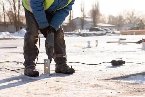 A worker in uniform mounts a metal structure in the foundation using a drill Stock Photos