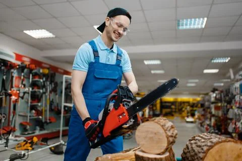 Worker in uniform testing chainsaw in tool store Stock Photos