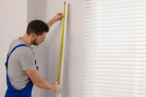 Worker in uniform using measuring tape while installing horizontal window b.. Stock Photos