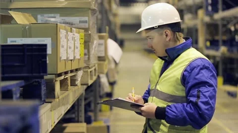 Worker in uniform on warehouse checking cargo and writing something on paper Stock Footage 61135958