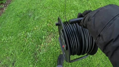 Worker unrolls power cable reel across lawn wearing black gloves walking Stock Footage 313250667