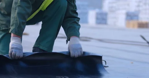 A worker unwinds a roll of ruberoid on a surface that needs to be isolated Video stock 119625563
