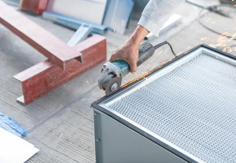 Worker use a grinder to cut the edges of the air filter metal box. Stock Photos
