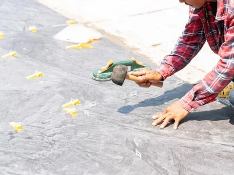 Worker use a rubber mallet to tap the tiles into level. Foto stock