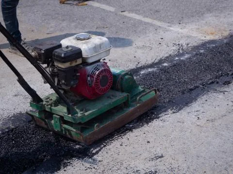 Worker use vibratory plate compactor compacting asphalt at road Stock Photos