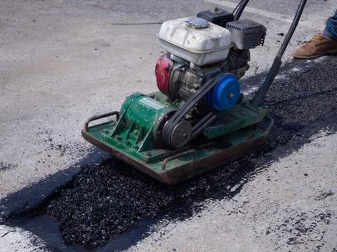 Worker use vibratory plate compactor compacting asphalt at road Stock-Fotos