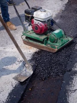 Worker use vibratory plate compactor compacting asphalt at road Stock Photos