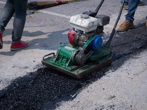 Worker use vibratory plate compactor compacting asphalt at road Stock Photos