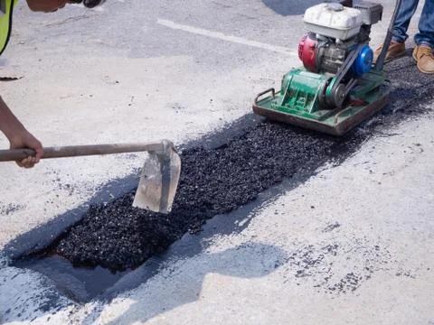 Worker use vibratory plate compactor compacting asphalt at road Stock Photos