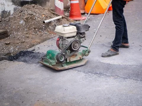 Worker use vibratory plate compactor compacting asphalt Foto stock