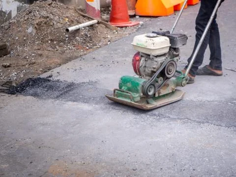 Worker use vibratory plate compactor compacting asphalt Stock Photos