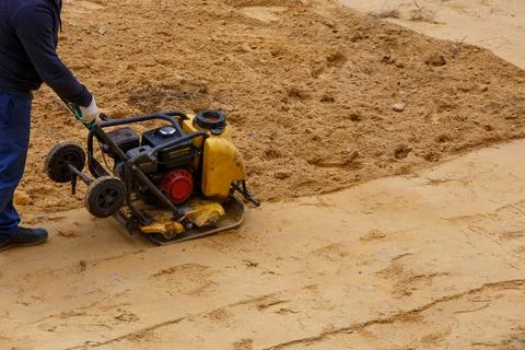 Worker in use vibratory plate compactor for compaction sand during path Stock Photos
