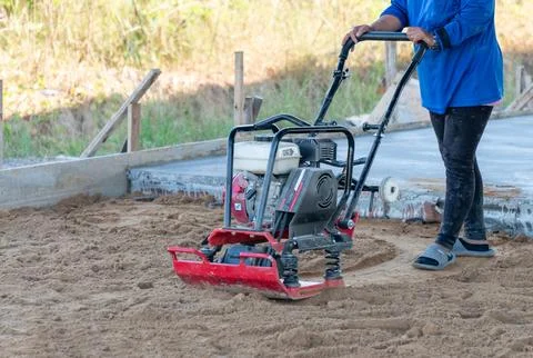 Worker in use vibratory plate compactor for compaction sand. Foto stock