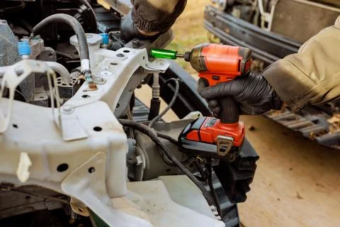 Worker uses cordless drill to work on vehicle metal frame in workshop setting Stock Photos