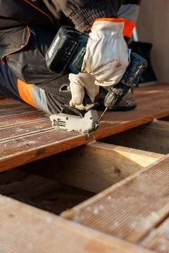 Worker uses drill and jigsaw to secure grooved timber decking boards Stock Photos