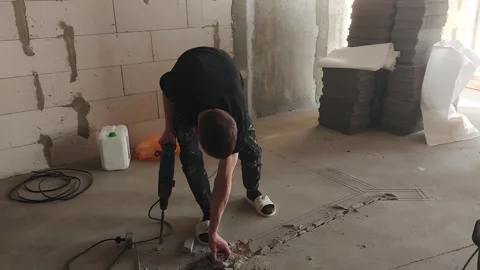 Worker uses drill to break concrete in construction area during daytime Stock Footage 329825905