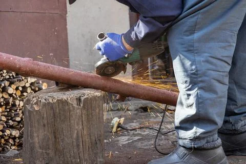 Worker uses an electric angle grinder to cut a rusted metal pipe on a woode.. Stock Photos