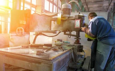 Worker uses equipment to shape materials inside a factory. Sunlight shines th Stock Photos