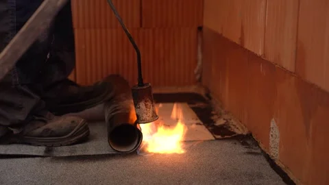 Worker uses flame torch to install bitumen sheet on house floor corner Stock Footage 311418596