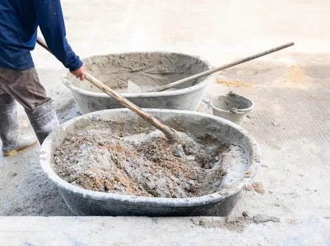 The worker uses a hoe to mix cement and sand. Stock Photos