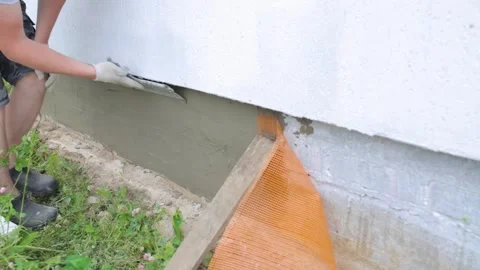 A worker uses a large trowel to putty the foundation of a house. Covering the Stock-Footage 250935690