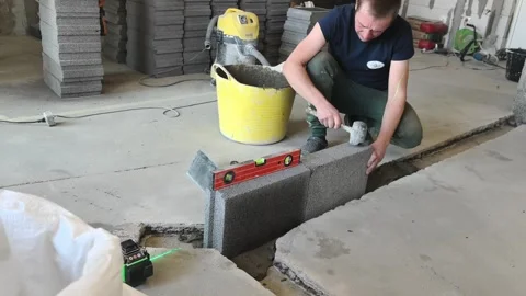 Worker uses a level to set concrete blocks in a construction area while preparin Video stock 332148720
