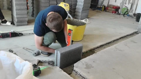 Worker uses level tool to adjust concrete blocks during construction in a buildi 스톡 동영상 332133132
