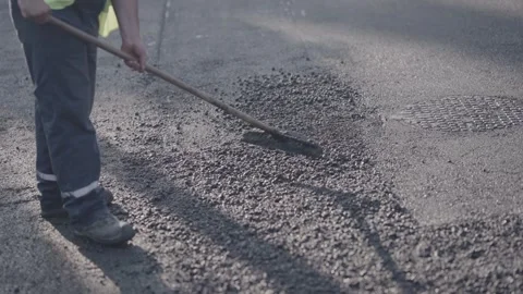 Worker uses manual tools to level a layer of fresh asphalt on a road Stock Footage 305105804