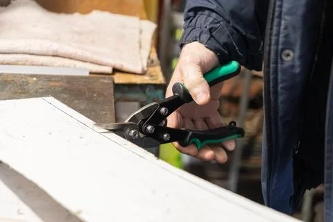 A worker uses metal snips to precisely cut a white plastic sheet at a workshop Stock Photos