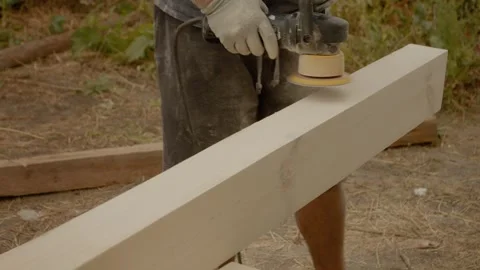 Worker uses orbital sander to smooth wooden beams in outdoor workspace Stock Footage 324672447