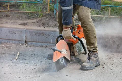 A worker uses a portable chainsaw and a diamond cutting disc to cut old aspha Stock Photos