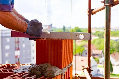 Worker uses a spirit level to control wall made of red blocks Stock Photos
