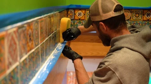 Worker uses a sponge to take off excess grout along a lower edge of tiles. Stock Footage 101434741