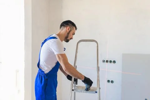 The worker uses a stepladder and a laser level Stock Photos