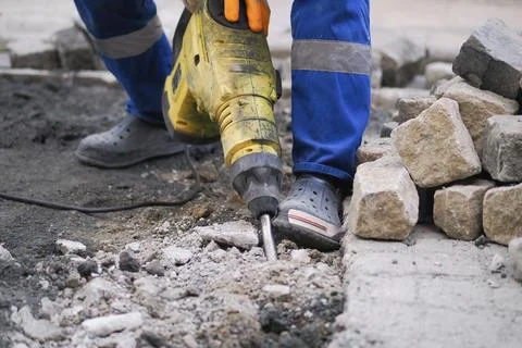 Worker uses a tool to break ground while laying stones at a construction site Stock Photos
