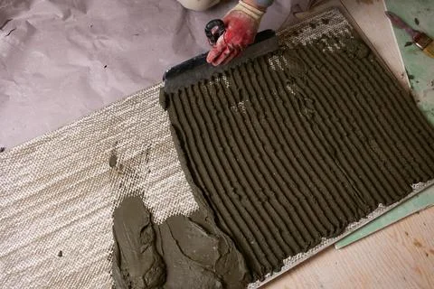 A worker uses a trowel to apply cement to a textured surface in a construct.. 库存照片