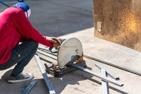 Worker using an abrasive chop saw machine to cut hollow structural steel pi.. Stock Photos